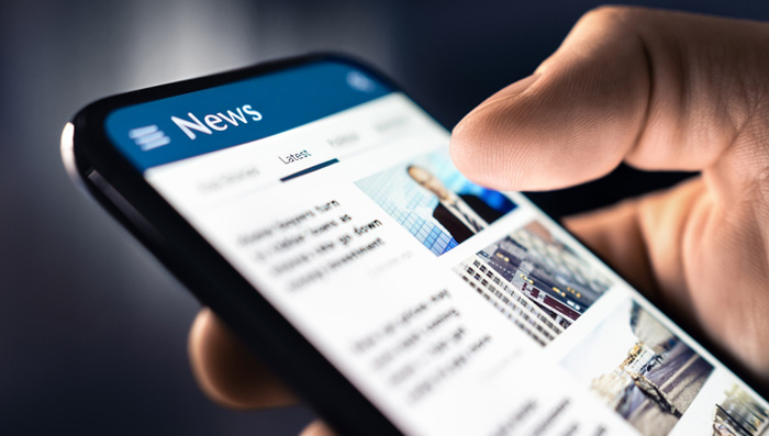 Close-up of a hand scrolling news headlines on a smartphone.